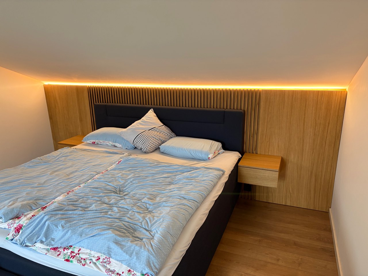 Schlafzimmer mit Wandverkleidung aus Eiche, indirekter Beleuchtung und schwebenden Nachttischen